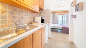 Una cocina con un lavamanos, armarios y un microondas. Hay una cama con vistas al exterior.