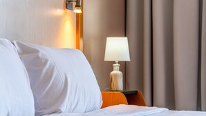 Una habitación de hotel con una cama bien hecha, una lámpara en una mesita de noche y una lámpara de pared.