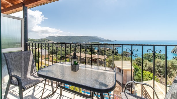 Un balcón con mesa y sillas, con vistas a un paisaje costero con montañas y el mar.