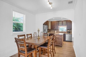 Un comedor con una mesa y sillas de madera, una cocina con armarios de madera y un refrigerador, y una ventana con persianas.