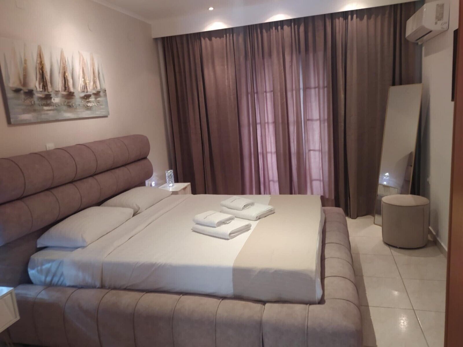A bedroom with a large bed, a nightstand, a mirror, and a painting on the wall.