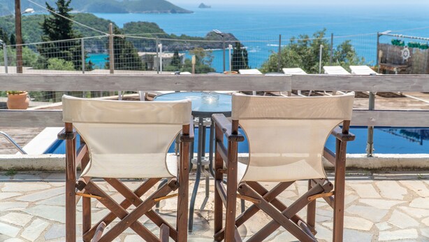 Une terrasse avec une table et des chaises, donnant sur une piscine et offrant une vue panoramique sur la mer et les montagnes.