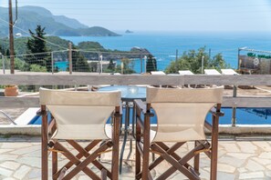 Una terraza con mesa y sillas, con vista a una piscina y un paisaje escénico del mar y las montañas.