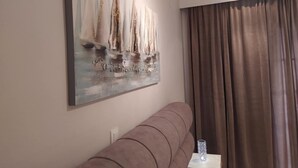 Un salon avec un canapé, un tableau représentant des voiliers et une fenêtre avec des rideaux.