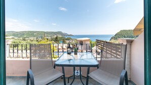 Un balcon avec une table et des chaises, donnant sur un paysage côtier avec des collines et une étendue d’eau.