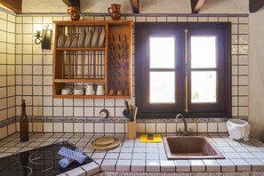 Una cocina con salpicadero de azulejos, estantes de madera, un ventanal de dos hojas y un lavamanos.