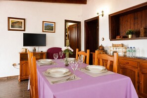 Un comedor con mantel púrpura, sillas de madera y un televisor montado en la pared.