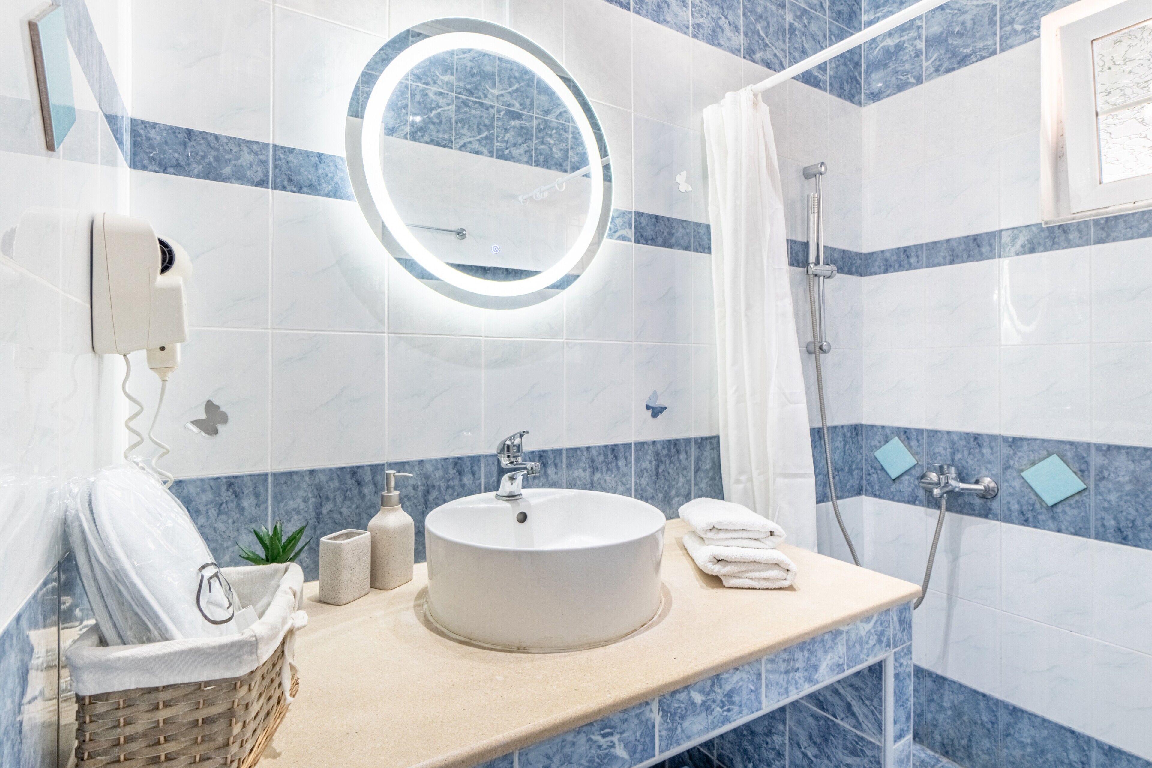 Een badkamer met een ronde spiegel, een wastafel, een douche en een handdoekrek.