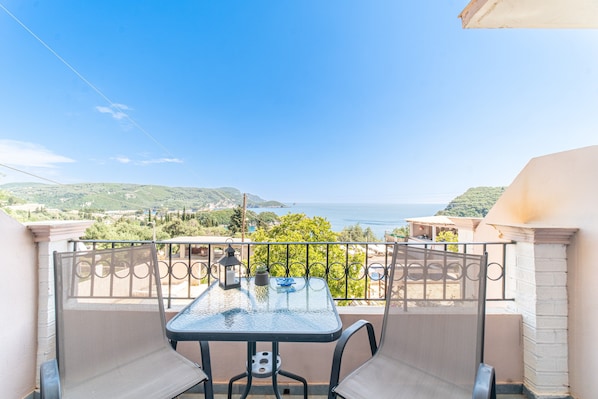 Uma varanda com mesa e cadeiras, com vista para colinas e o mar.