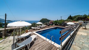 Une piscine entourée d’une terrasse en bois, de chaises longues et de parasols.