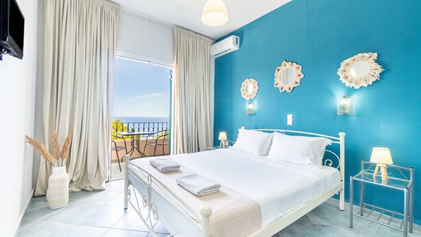 Une chambre à coucher avec un lit, des rideaux, un balcon donnant sur une vue agréable et des miroirs décoratifs sur les murs.