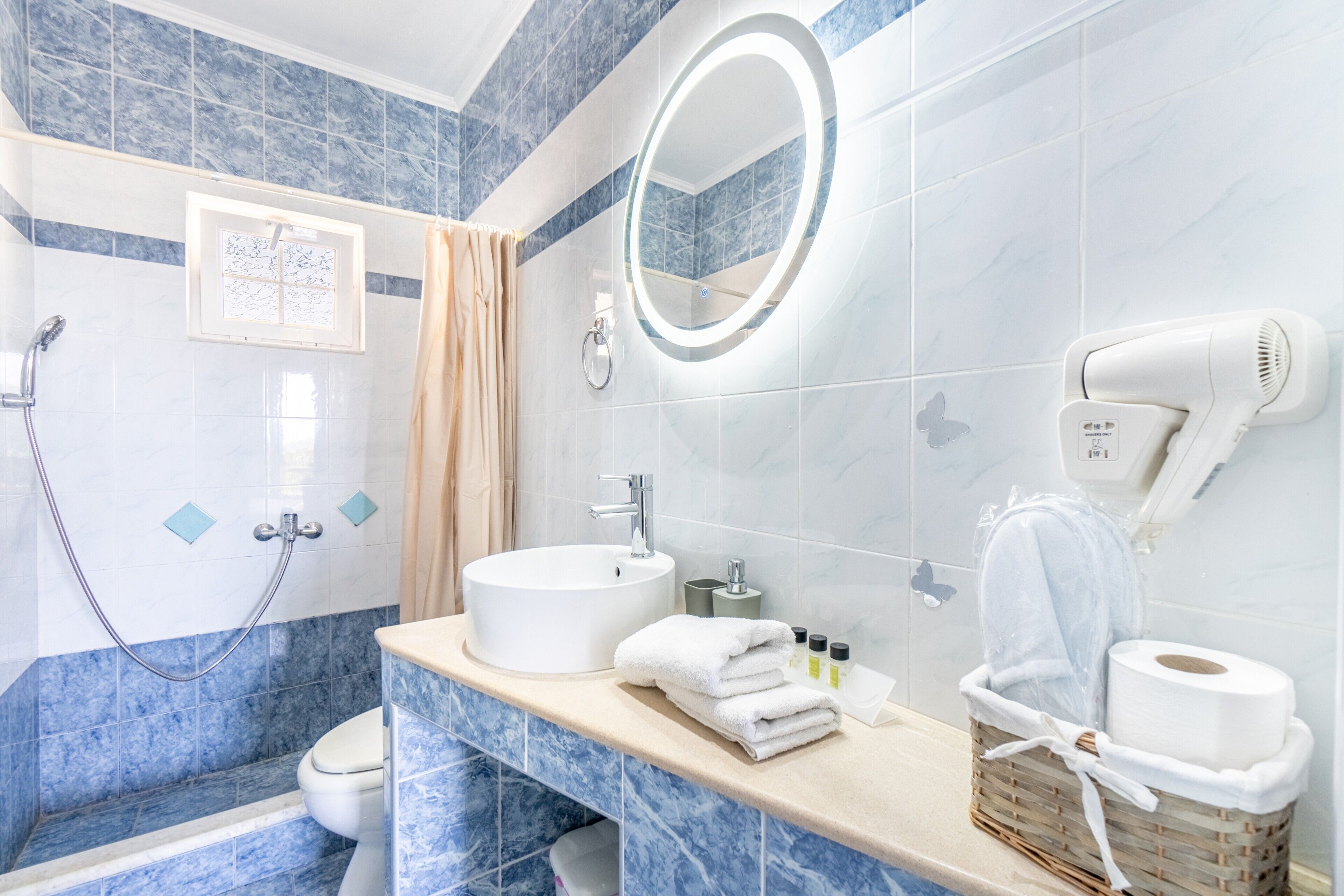 A bathroom with a sink, mirror, shower, toilet, and a hairdryer on the wall.
