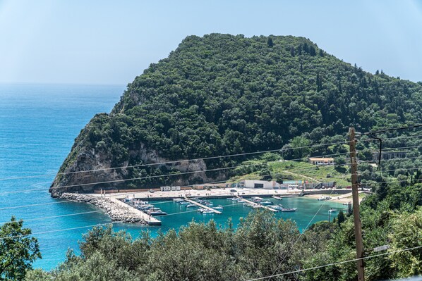A coastal marina with boats docked, surrounded by lush greenery and a mountainous backdrop.