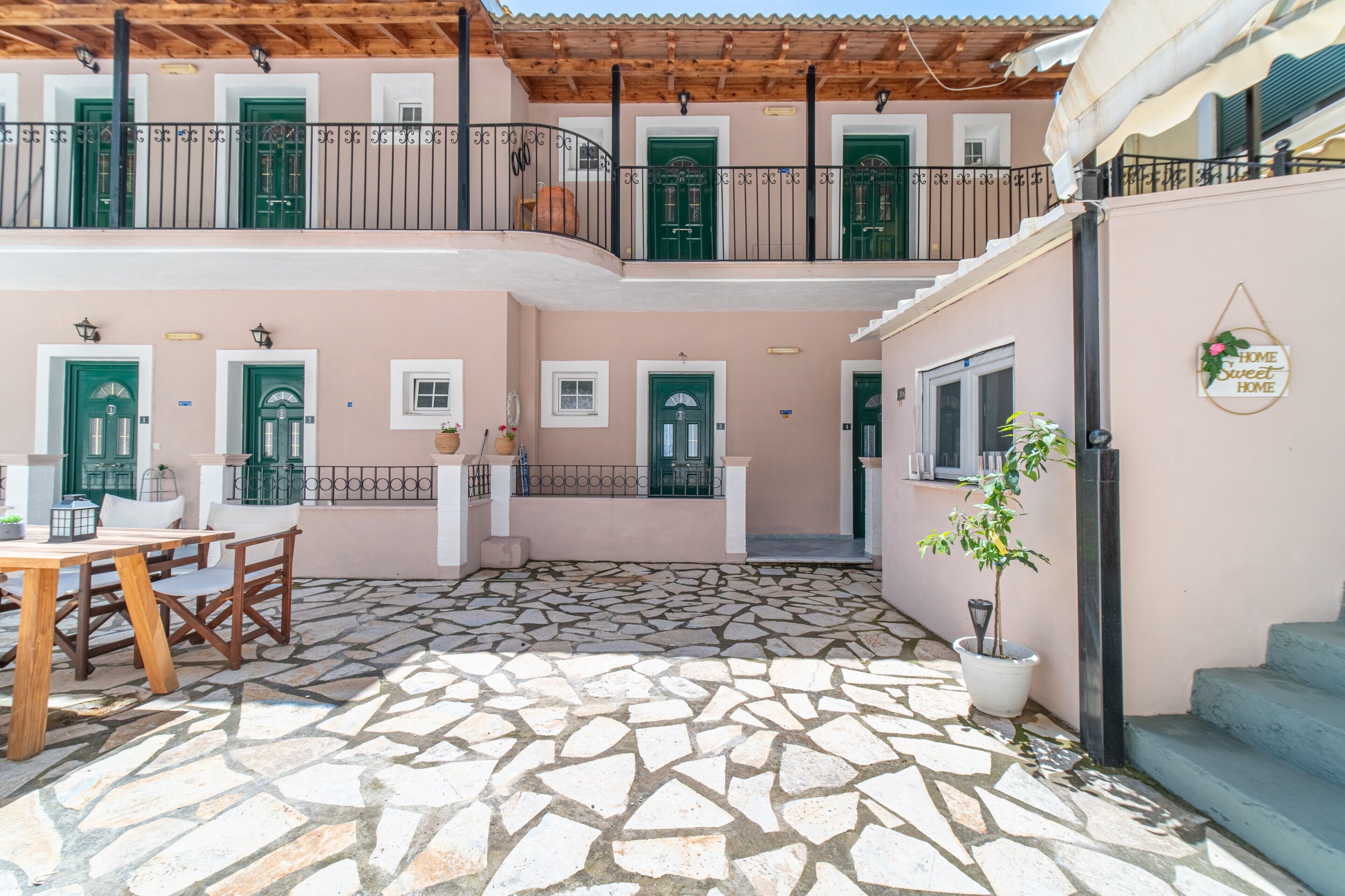Un immeuble à plusieurs étages doté d’une cour dallée de pierres, de portes vertes et d’un balcon orné d’une rambarde en métal.