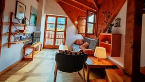 A cozy room with wooden beams, a sofa, a chair, a table, and a bookshelf.