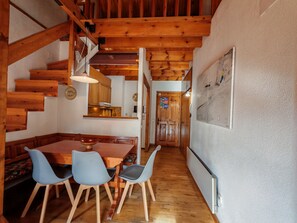 A wooden staircase leading to a loft bedroom, a dining area with a wooden table and chairs, and a kitchen with wooden cabinets.