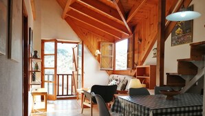A wooden interior with a dining table, chairs, a sofa, and a staircase.
