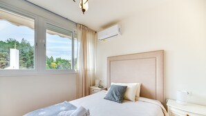 Une chambre d’hôtel équipée d’un lit, d’une table de chevet, d’un appareil de climatisation et d’une fenêtre donnant sur un paysage verdoyant.