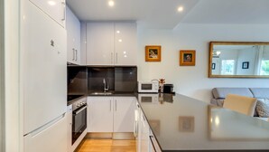 Une cuisine moderne avec des armoires blanches, une hotte de cuisinière en acier inoxydable, un four à micro-ondes et un grand îlot central doté d’un plan de travail foncé.