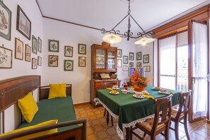Ein Zimmer mit einem Bett, einem Esstisch mit Stühlen, einer Chandelüster und gerahmten Bildern an den Wänden.