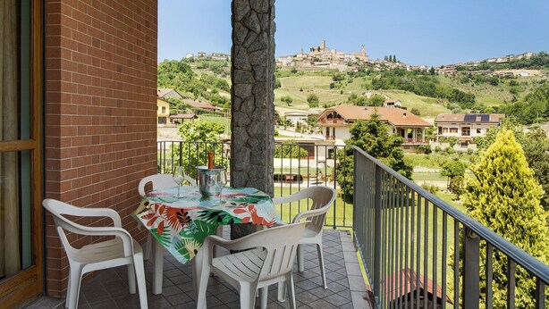 A balcony with a table and chairs, a stone pillar, and a view of a hillside town. - Holiday apartment "Clematis" in Piedmont, with shared pool, garden and sauna (Cisterna d'Asti)