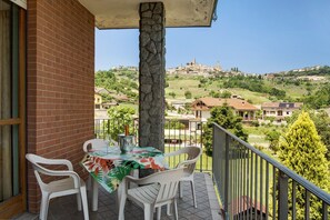 Un balcón con una mesa y sillas, un pilar de piedra, y vistas a un pueblo en la ladera.