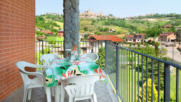A balcony with a table and chairs, overlooking a hillside with buildings.
