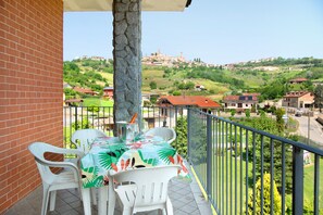 A balcony with a table and chairs, overlooking a hillside with buildings. - Holiday apartment 'Glicine' in Piedmont, with shared pool, garden and sauna (CISTERNA D'ASTI)