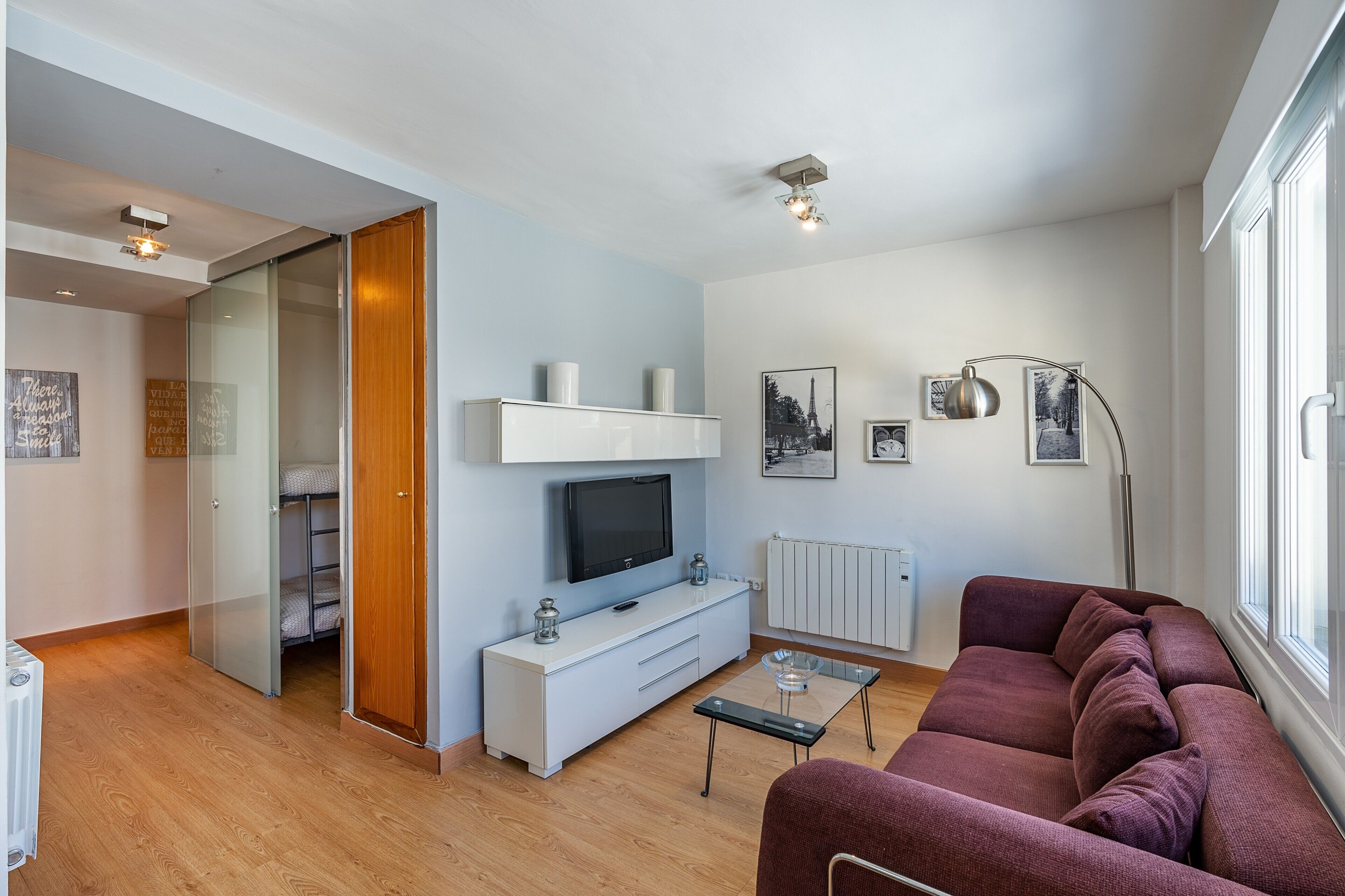 A modern living room with a sofa, TV, glass cabinet, and artwork on the wall.