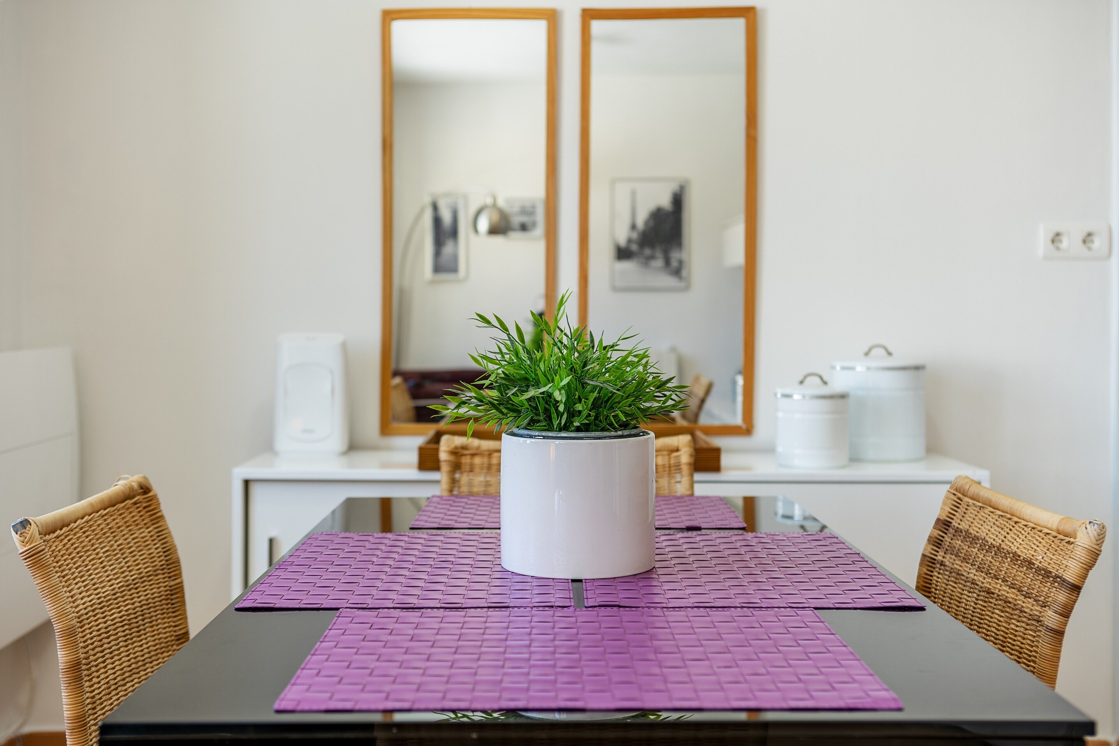 Una mesa de comedor con una planta en maceta, salvamanteles morados y sillas de mimbre.