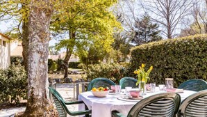 Un espace de restauration en plein air avec une table dressée pour quatre personnes, entourée de chaises vertes.