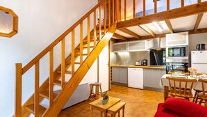 Une cuisine spacieuse avec des poutres en bois, un coin repas avec un canapé rouge et un escalier menant à un niveau supérieur.