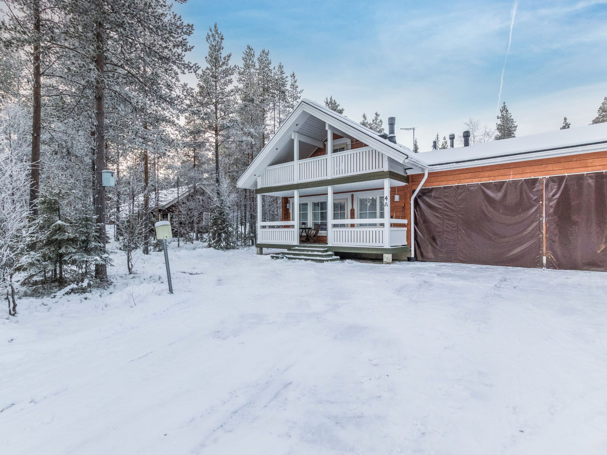 A two-story cabin with a balcony, surrounded by snow-covered trees.