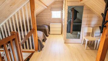 A cozy attic bedroom with a wooden staircase, a bed, a dresser, and a view of a staircase leading to another level.