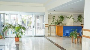 A hotel lobby with a reception desk, potted plants, and a glass door entrance.