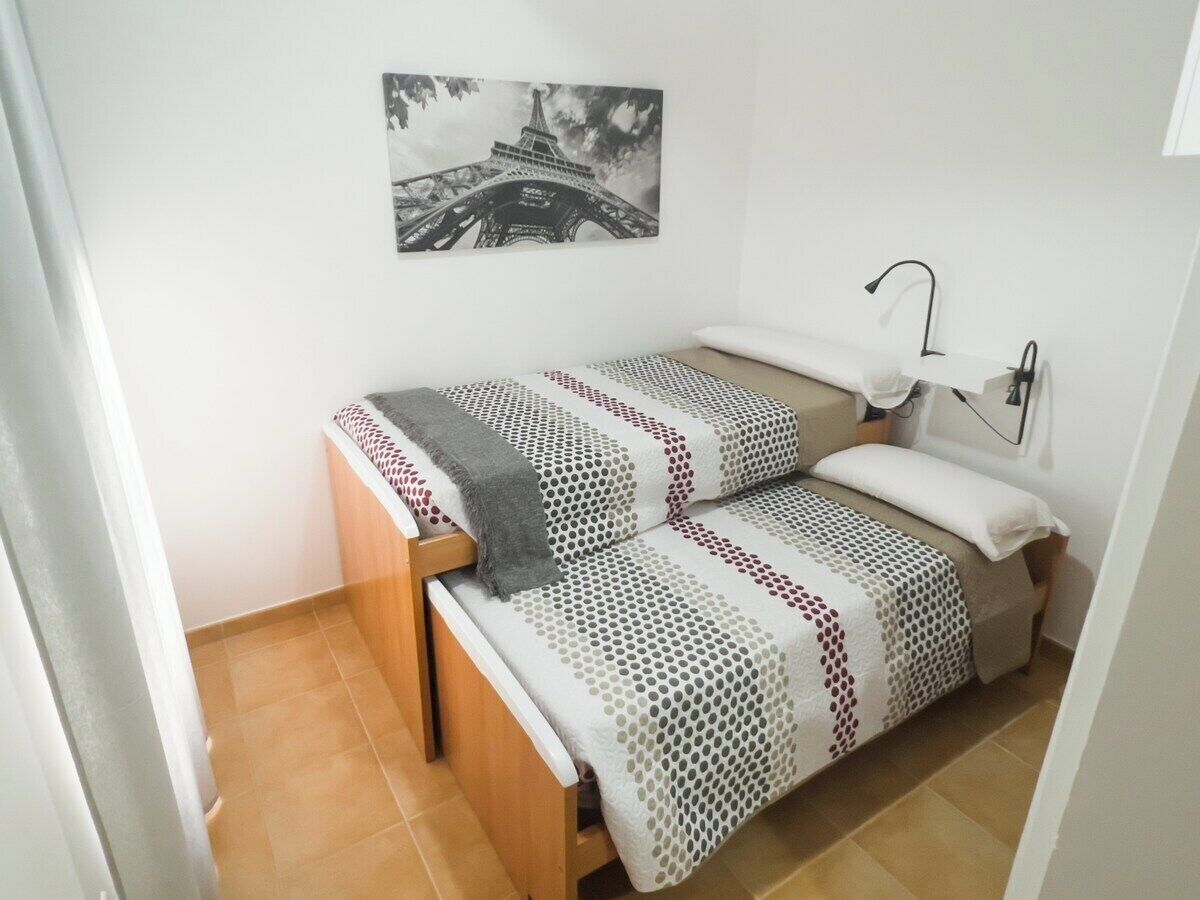 A small, neatly arranged bedroom with a bed, a nightstand, and a wall-mounted lamp.