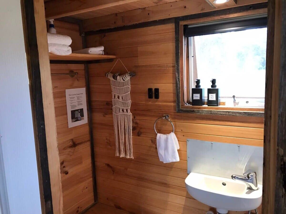 Une salle de bain rustique, aménagée dans une cabane en bois, avec un lavabo, un porte-serviettes et une fenêtre sur le rebord de laquelle sont posées des bouteilles.