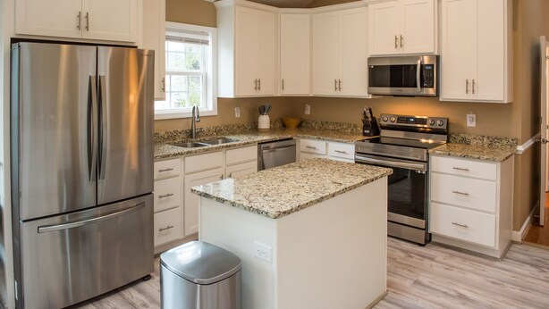 A modern kitchen with white cabinets, stainless steel appliances, granite countertops, and a central island.