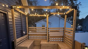 A wooden deck with a table and benches, string lights, and a wooden pergola.