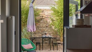 Une vue d’une terrasse avec une table dressée pour deux personnes, une chaise verte et un parasol suspendu.