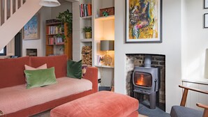 A cozy living room with a red sofa, a fireplace, bookshelves, and a staircase. - Beautifully designed, stylish holiday home, seconds from the beach (Walmer, Deal)