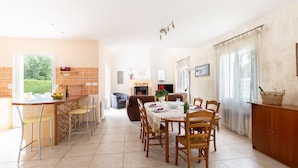 Une cuisine spacieuse avec un coin repas, comprenant un îlot central en briques, des chaises en bois et une grande fenêtre.