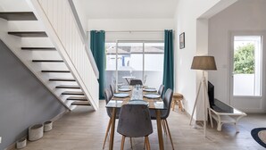 A modern dining area with a glass table, chairs, and a view through large windows.