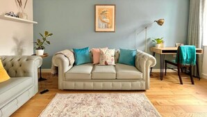 Una sala de estar con un sofá color beige, un tapete estampado, un escritorio con una silla y una lámpara de pie.