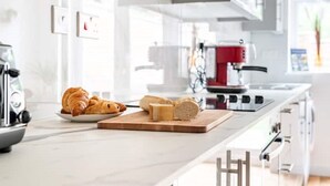 Una cocina moderna con encimera de mármol, cafetera, estufa roja y tabla de cortar con pan y queso.