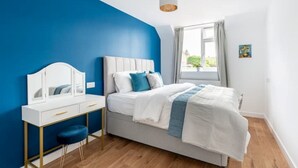 Un dormitorio con cama, una mesita de noche con espejo y una ventana con cortinas.