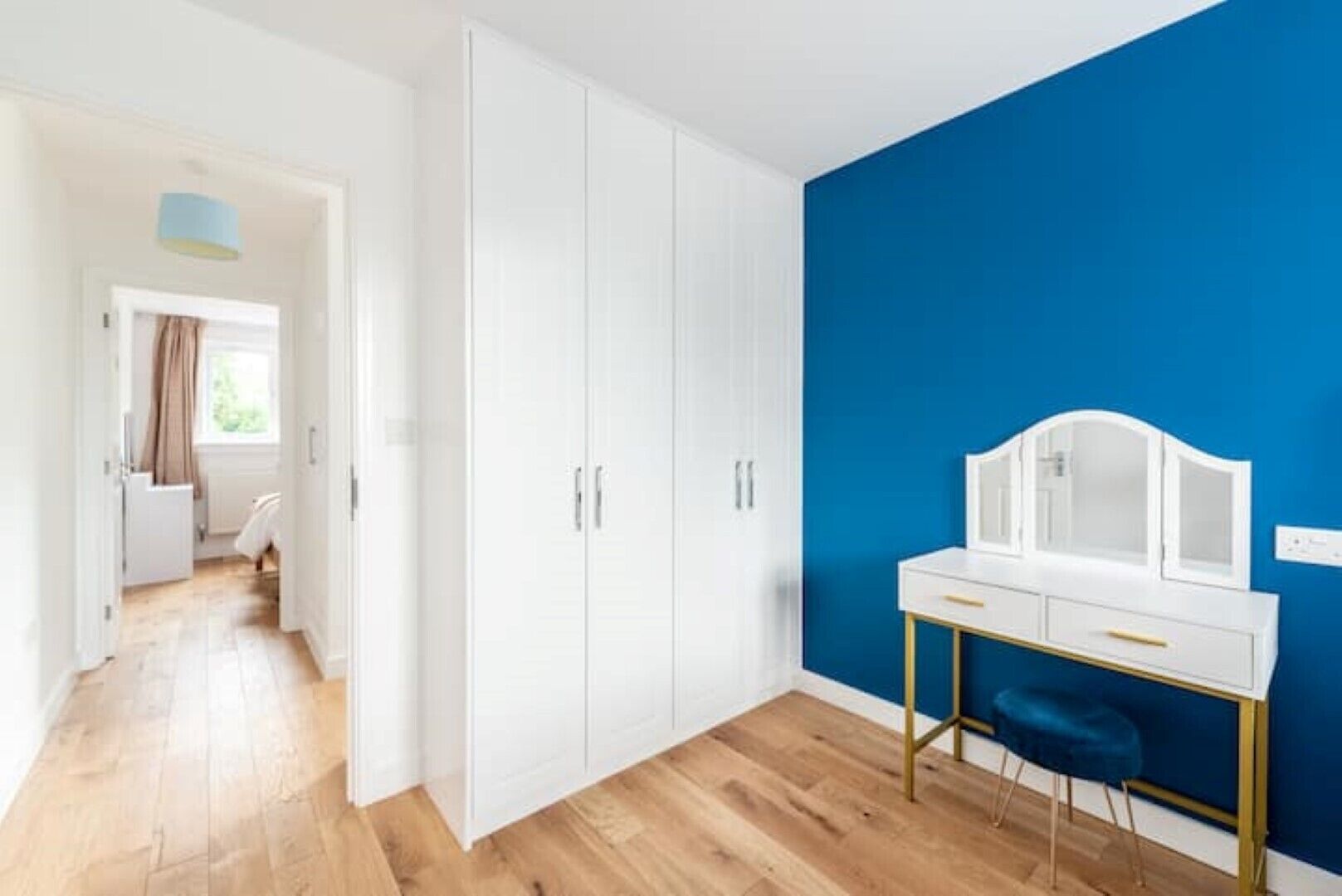 Une pièce avec un plancher en bois, une armoire blanche et un mur d’accent bleu.