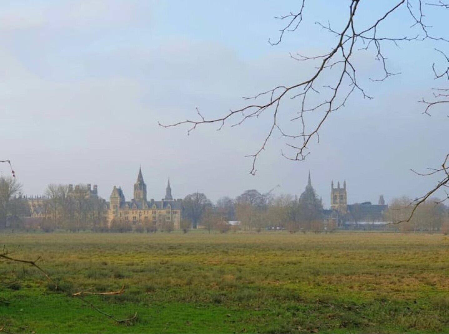 A large, historic building complex with multiple towers and spires, surrounded by open fields.