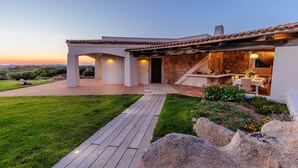 Une maison moderne avec une façade en pierre, une terrasse en bois et une pelouse bien entretenue.