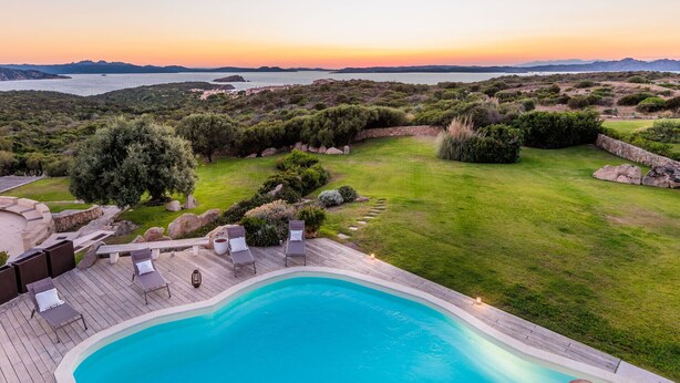 Un espace piscine offrant une vue sur la mer et les collines au coucher du soleil.